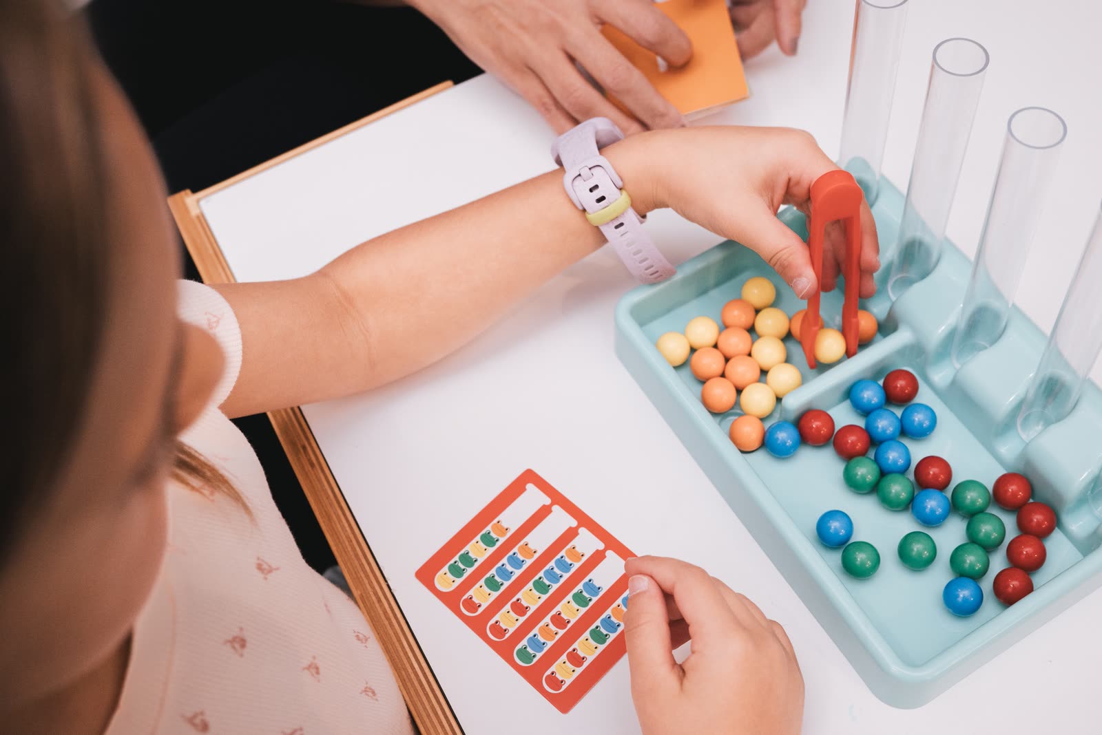 Overhead view of a child using tweezers in a fine-motor sorting game