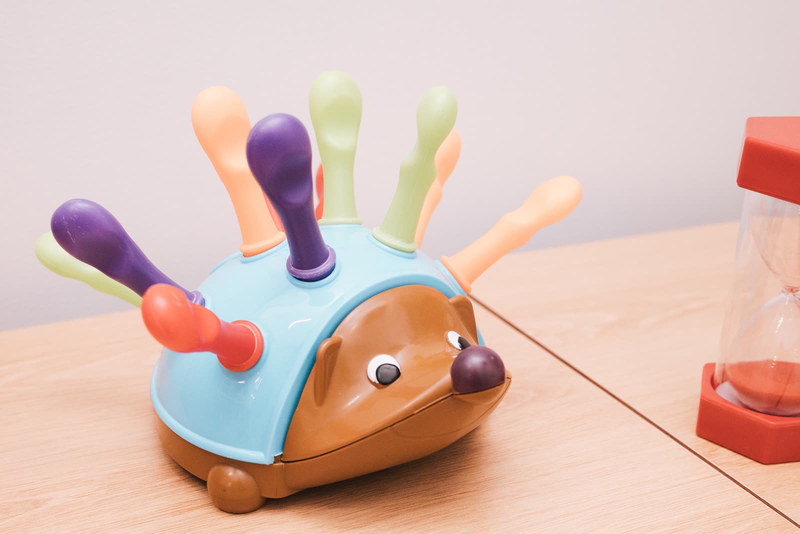 A fine-motor hedgehog spike toy beside a sand timer